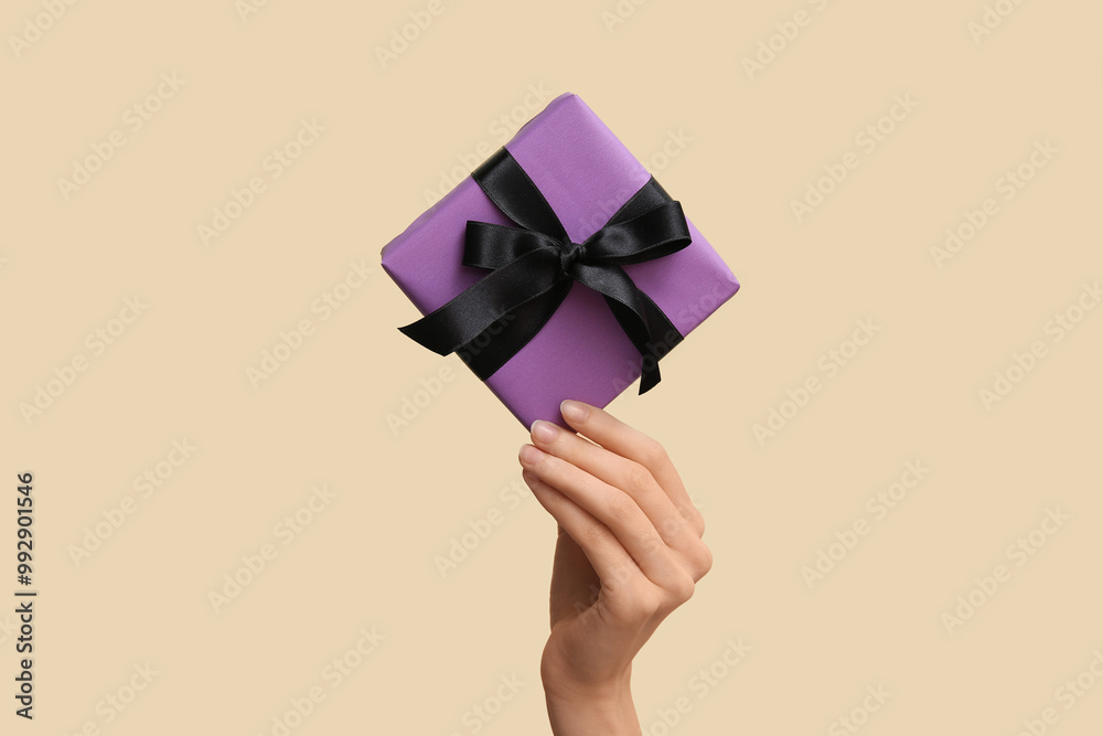 Female hand with Halloween gift box on beige background