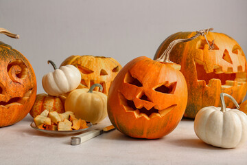 Different Halloween carved pumpkins and knife on white table near grey wall