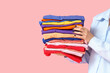 © Pixel-Shot - Young woman with stack of colorful clothes on pink background, closeup