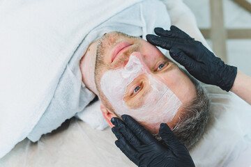 A cosmetologist cleans the skin of a man's face. A man does facial procedures in a cosmetic clinic. Male cosmetology.