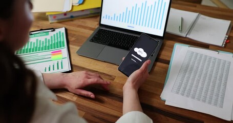 Businesswoman synchronizes mobile phone and laptop data using new program. Lady sitting at table with documents and statistics transfers data to cloud for information security