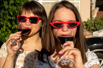 Wall Mural - Portrait of a two young woman in sunglasses drinking wine	