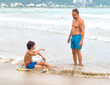© kravik93 - Father and teenager are chatting on the sandy sea beach. They are smiling and having a conversation about riding the waves. Family active vacation concept