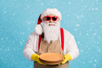 Wall Mural - Photo of pensioner old man grey beard hold clean dishes restaurant service waiter half-time wear santa x-mas costume apron rubber glove suspender sunglass cap isolated blue color background