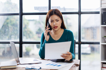 Wall Mural - Asian woman entrepreneur busy with her work in the office. Young Asian woman work on desk laptop phone while planning sales, research or financial strategy in company
