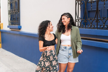 Two Latin women smiling and walking together on a city street