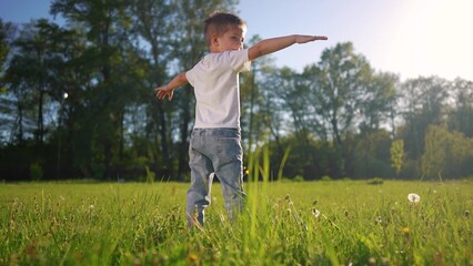 small boy playing in the park. family park outside and nature concept. a little boy in a white T-shirt stands in the park with his arms outstretched and rejoices lifestyle