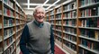© Arceli - Joyful elderly Caucasian man wearing a sweater in a library with bookshelves