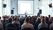 © M2A - Business and entrepreneurship conference. Presenter delivering a speech at a business event. Attendees seated in the conference hall. Rear view of an unidentifiable audience member.