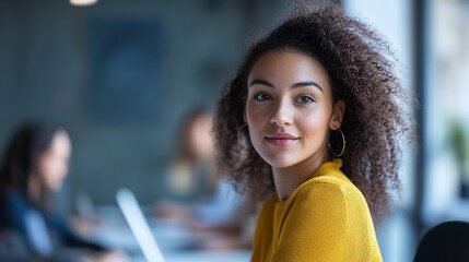 Wall Mural - A woman with curly hair smiles while seated in a modern workspace, engaging with her surroundings and exuding confidence and warmth.