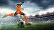 © master1305 - Athletic young African-American man in orange uniform, soccer player in motion on outdoor arena, dynamically playing, showing readiness to score goal. Concept of sport, tournament, competition, game