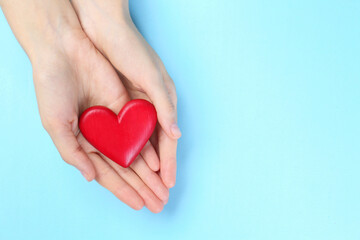 Wall Mural - Woman holding red heart on light blue background, top view. Space for text