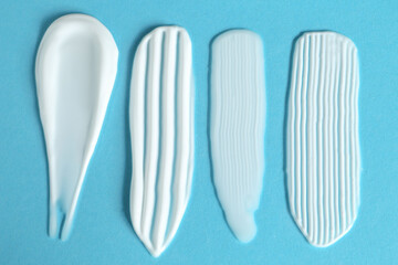 Sticker - Smears of cosmetic products on light blue background, flat lay