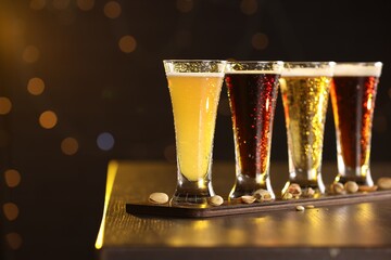 Poster - Glasses with different types of beer and pistachios on wooden table against blurred lights, closeup. Space for text