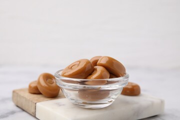 Wall Mural - Tasty hard toffee candies in bowl on white table, closeup