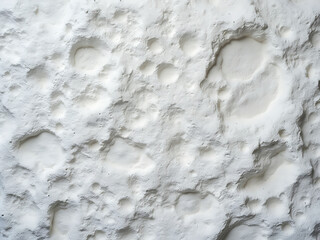 A close-up of a textured white surface with craters and indentations, resembling a lunar landscape or a weathered rock face.