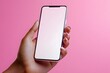 © Punprapa - A hand of a Black woman holding up a blank screen smartphone against a pink background
