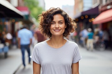 Canvas Print - Portrait of a satisfied woman in her 30s dressed in a casual t-shirt while standing against bustling city street background