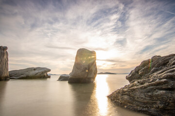 View through rocks on a sandy beach into the sunset. Landscape shot with a view to the horizon over the wide sea on the coast of Ouranoupoli, Thessaloniki, Central Macedonia, Greece