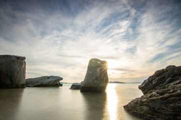 View through rocks on a sandy beach into the sunset. Landscape shot with a view to the horizon over the wide sea on the coast of Ouranoupoli, Thessaloniki, Central Macedonia, Greece