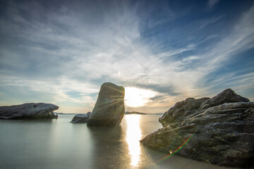 View through rocks on a sandy beach into the sunset. Landscape shot with a view to the horizon over the wide sea on the coast of Ouranoupoli, Thessaloniki, Central Macedonia, Greece