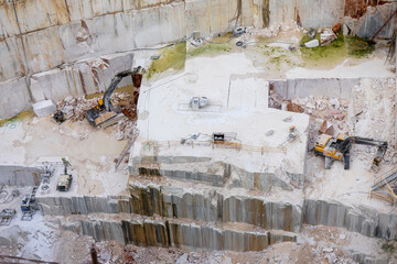 Machines working in the depths of a marble quarry in Vila Viçosa, Alentejo, Portugal. Industrial equipment extracting marble blocks amidst a rugged landscape of stone and dust.