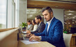 © Studio Romantic - Serious business people sitting in a row and working on laptop in modern open plan office sitting at same desk. Company employees wearing suits typing on computers on their workplace.