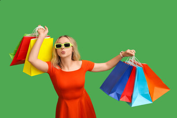 Canvas Print - Young woman in sunglasses with shopping bags on green background