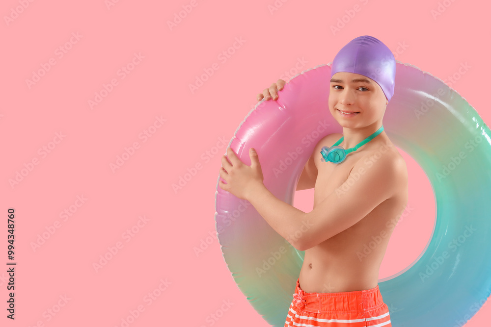 Cute little happy boy with swimming cap, inflatable ring and goggles on pink background