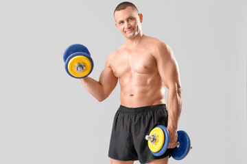 Canvas Print - Muscular male bodybuilder exercising with dumbbells on grey background