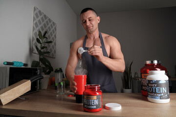 Poster - Handsome muscular man pouring protein powder into bottle for shake in kitchen