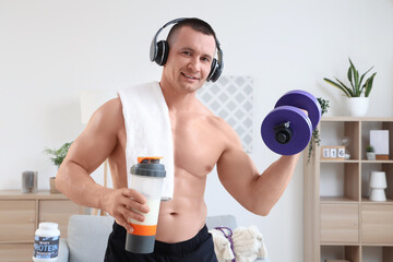 Sticker - Young muscular man in headphones with protein shake and dumbbell at home