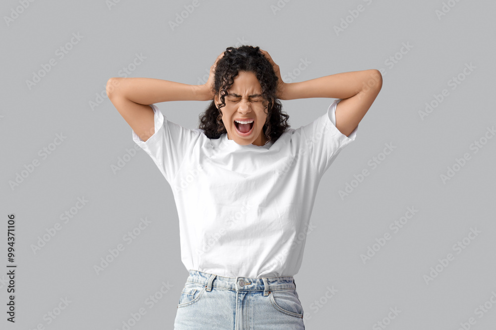 Young African-American woman having panic attack on grey background