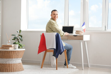 Wall Mural - Young man with laptop and flag of France sitting at table in home office