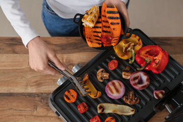 Woman cooking tasty vegetables on modern electric grill in kitchen