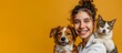 © Vitalii Shkurko - A joyful female veterinarian smiles while holding a content dog and curious cat against a vibrant yellow background, banner, With copy space for text.