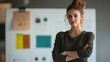 © Amanda - Confident young woman with crossed arms stands in front of a creative workspace filled with colorful design materials during daylight