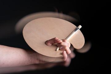 Close up of man's hand holding round wooden palette and paint brushes with motion effect