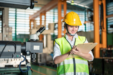 helmet, mechanic, safety, manufacturing, machinery, examining, foreman, inspection, inspector, hard hat. A woman wearing a yellow helmet and a green vest is looking at a clipboard.