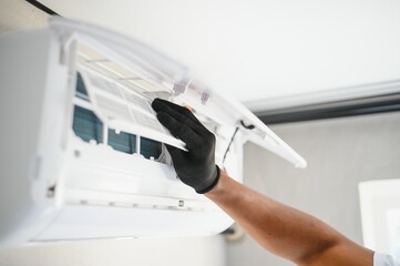 Poster - the hands of an african worker insert a new filter into the air conditioner