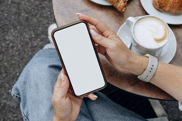 Mockup woman's hand holding using smart phone with white blank screen at coffee shop, mobile app design and advertising, online marketing