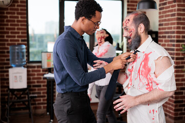 African american director on set arranging tie on actor portraying zombie in horror movie. Filmmaker doing finishing touches on man costume playing undead creature in office for thriller film