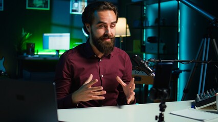 Wall Mural - Influencer talks in front on smartphone attached to tripod and high quality mic in studio, discussing with viewers. Man using mobile phone and professional gear to record social media video, camera B