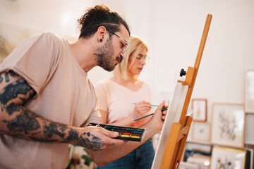 Wall Mural - Young creative couple painting together on easel at art studio.