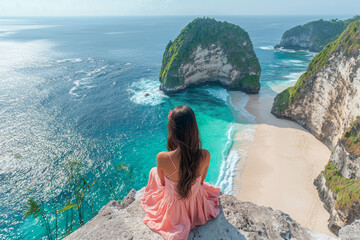 Wall Mural - A girl in pink dress sits on edge of cliff, overlooking stunning beach with turquoise waters and lush greenery. serene landscape evokes sense of peace and wonder