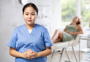 Portrait of young qualified doctor in uniform against background of lying patient