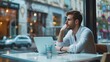 © Qstock - Young Man Working Remotely in CafÃ©, Using Laptop, and Looking Thoughtful