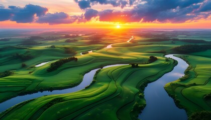 Wall Mural - Serene sunrise over a winding river flowing through vibrant green fields beneath a colorful sky with scattered clouds