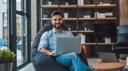 Poster - happy young businessman sitting in bag chair in modern office working on laptop