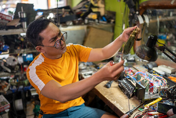 spectacled repairman working on electronic circuitry near a lamp at workshop